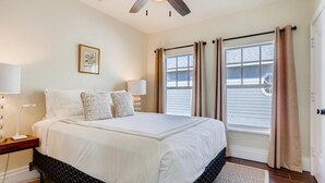 Ein Schlafzimmer mit einem großen Bett, zwei Nachttischlampen, einem Deckenventilator und einem Fenster mit Vorhängen.