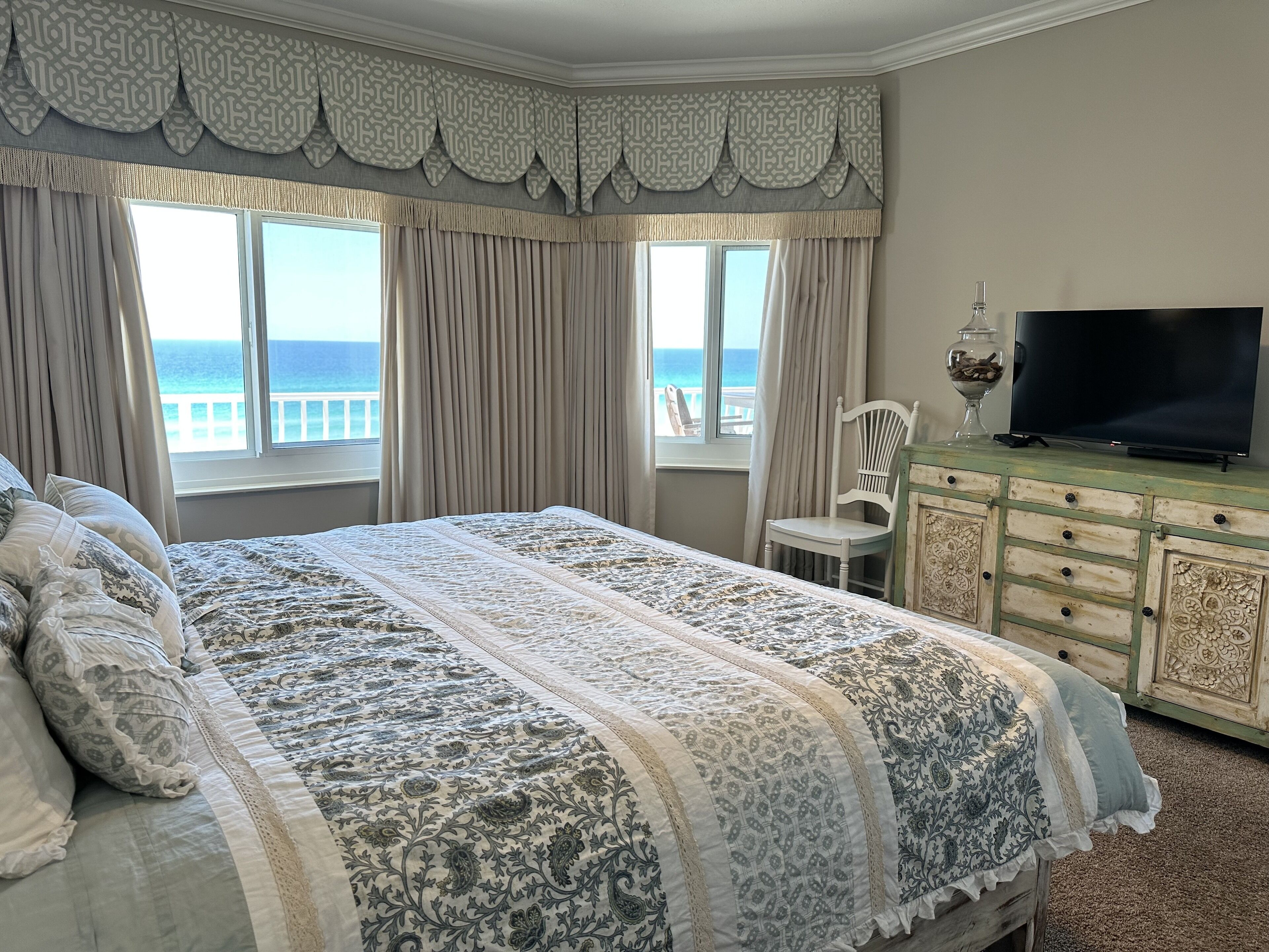 Un dormitorio con una cama grande, televisión, una silla y vista al océano.