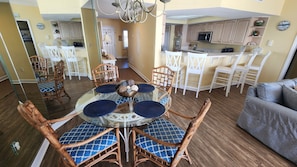 A dining area with a round glass table, wicker chairs, and a blue patterned rug.