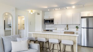 A modern kitchen with white cabinets, stainless steel appliances, and a bar area with stools. - Waikiki Golden Gem: 1 Br w/ Free Parking (Honolulu)