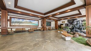 A spacious lobby with stone flooring, wooden benches, a large mural, and a waterfall feature. - Waikiki Golden Gem: 1 Br w/ Free Parking (Honolulu)