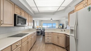 A modern kitchen with wooden cabinets, stainless steel appliances, and a large window offering a view of the ocean. - Coral Reef Unit#706 (Beachfront 4 bedroom 3 bath condo on the 7th floor) (Panama City Beach)