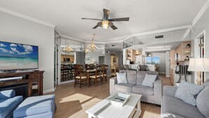 A spacious living room with a large flat-screen TV, a ceiling fan, and a dining area with wooden furniture. - Coral Reef Unit#706 (Beachfront 4 bedroom 3 bath condo on the 7th floor) (Panama City Beach)