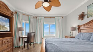 A hotel room with a bed, a desk, a chair, a television, a ceiling fan, and a window with curtains. - Coral Reef Unit#706 (Beachfront 4 bedroom 3 bath condo on the 7th floor) (Panama City Beach)