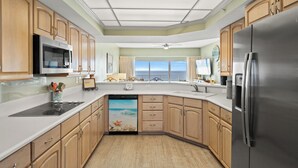A kitchen with wooden cabinets, a stainless steel refrigerator, a dishwasher, and a large window with a view of the ocean.