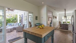 Un'ampia cucina con isola in legno, una zona pranzo con tavolo e sedie, e vista su un giardino rigoglioso attraverso ampie finestre.