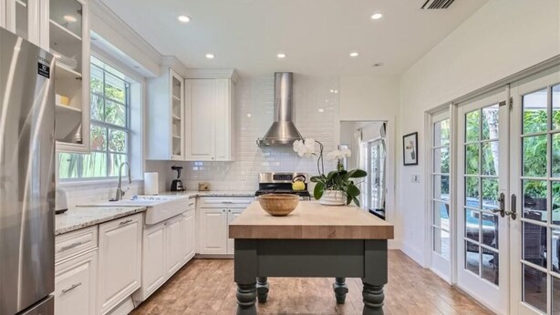 Una cucina moderna con mobili bianchi, un'isola in legno e un frigorifero in acciaio inossidabile.
