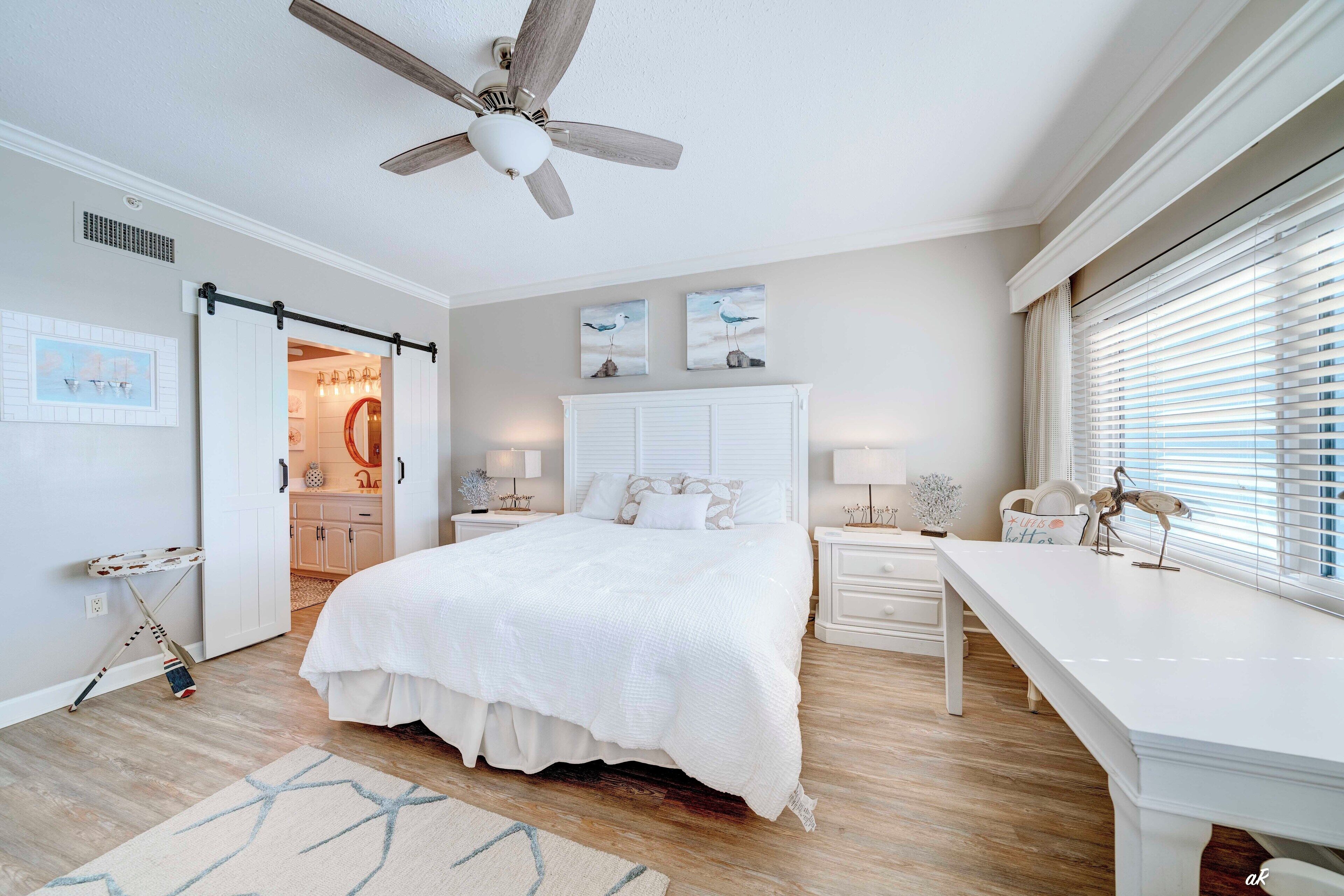 Un dormitorio con una cama grande, ventilador de techo, escritorio y ventana con persianas.