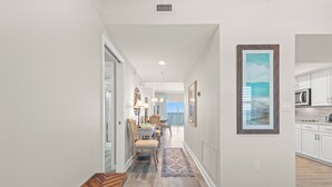 A hallway with a wooden bench, a dining area with chairs and a table, and a kitchen with white cabinets and a microwave. - Coral Reef, Unit #1102 (Beachfront 2 bedroom 2 bath condo on the 11th floor) (Panama City Beach)