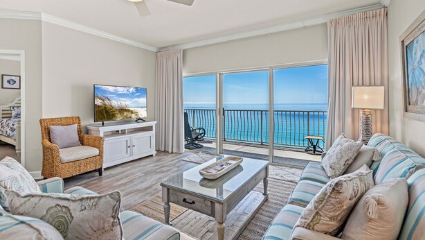 A spacious living room with a large window offering a view of the ocean, a ceiling fan, a television, and a comfortable seating area. - Coral Reef, Unit #1102 (Beachfront 2 bedroom 2 bath condo on the 11th floor) (Panama City Beach)
