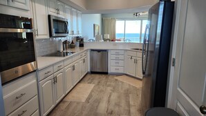 A modern kitchen with stainless steel appliances, white cabinetry, and a view of the sea through a large window. - Coral Reef Unit #1405 Beachfront 2 bedroom 2 bath condo on the TOP floor!!! (Panama City Beach)