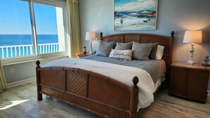 A bedroom with a large bed, two bedside tables, a painting, and a view of the ocean. - Coral Reef Unit #1405 Beachfront 2 bedroom 2 bath condo on the TOP floor!!! (Panama City Beach)
