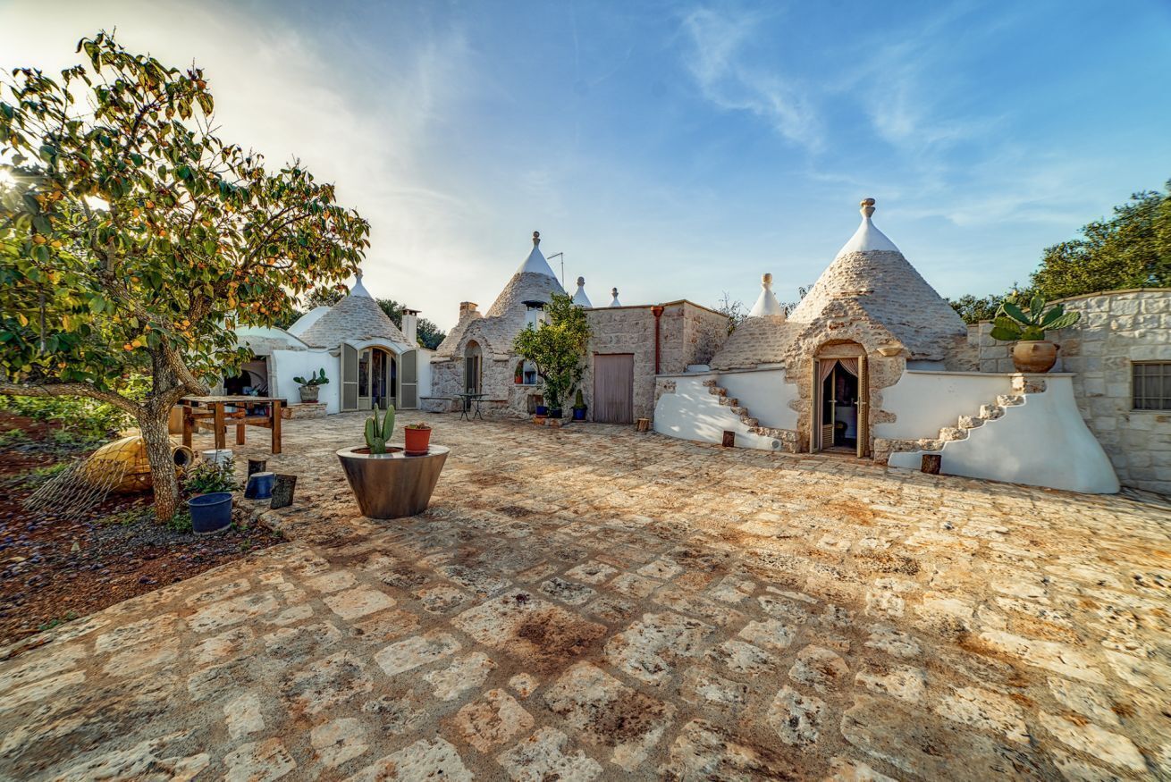 A courtyard with stone buildings, a tree, and potted plants.