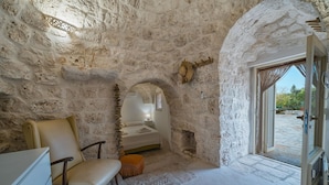 A stone-walled room with a bed, a chair, and a small table.