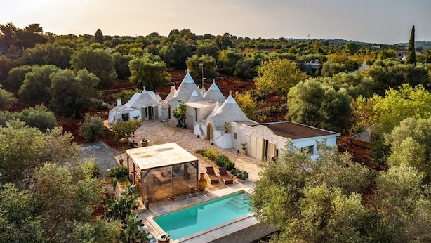 A villa with a swimming pool, surrounded by olive trees and a hilly landscape.