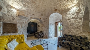 A stone-walled room with a yellow sofa, a patterned sofa, and a glass coffee table.