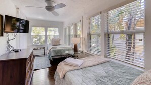 A bedroom with two beds, a ceiling fan, a TV, and large windows with blinds. - The Periwinkle House 4bd 2ba Sleep 8 (West Palm Beach)