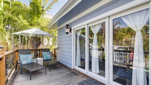 A wooden deck with outdoor furniture, a pergola with umbrellas, and a large sliding glass door. - The Periwinkle House 4bd 2ba Sleep 8 (West Palm Beach)