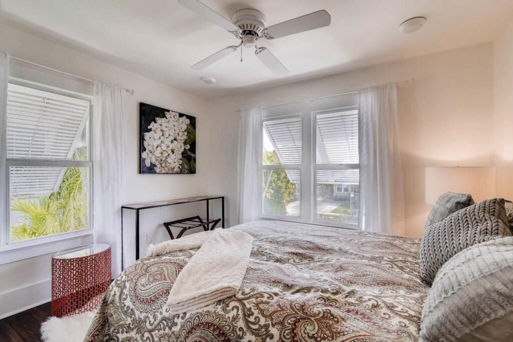 A bedroom with a large bed, a ceiling fan, and a view of greenery outside.