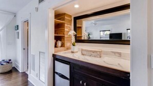 A modern kitchen with a marble countertop, dark cabinets, and a large mirror above the sink. - The Periwinkle House 4bd 2ba Sleep 8 (West Palm Beach)