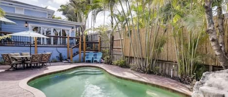 A swimming pool with a curved edge, surrounded by a wooden fence and palm trees.
