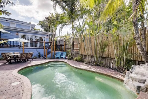 A swimming pool with a curved edge, surrounded by a wooden fence and palm trees.
