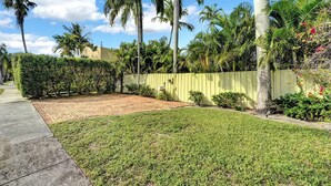 A well-maintained garden with a paved patio, palm trees, and a yellow fence.