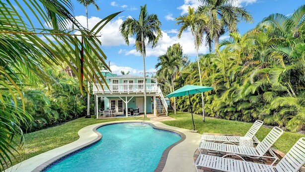 A swimming pool with a curved edge, surrounded by palm trees and a two-story building with a balcony.