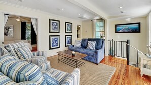 A spacious living room with a blue sofa, striped armchairs, a wooden coffee table, and framed artwork on the walls.