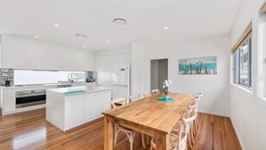 A modern kitchen with white cabinetry, a wooden dining table, and a view of the sea through the window. - Pearls on Sapphire Beach (Sapphire Beach)