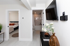 A modern hotel room with a bed, a desk, a TV, and a bathroom visible through an open door.