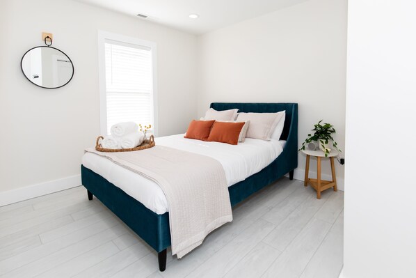 A bedroom with a bed, a bedside table, a mirror, and a window.