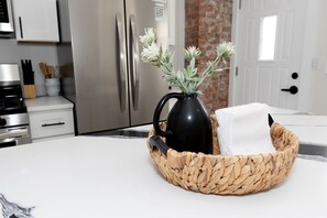 A kitchen with a white countertop, a woven basket containing a black pitcher and a white cloth, and stainless steel appliances.