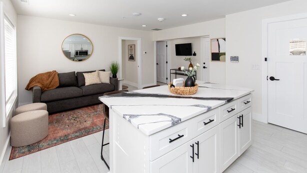 A modern kitchen with white cabinets, a marble countertop, and a central island. There is a dark-colored sofa and a round mirror on the wall. - New! Adjoining Suites - Sleeps 12! (Sandusky)