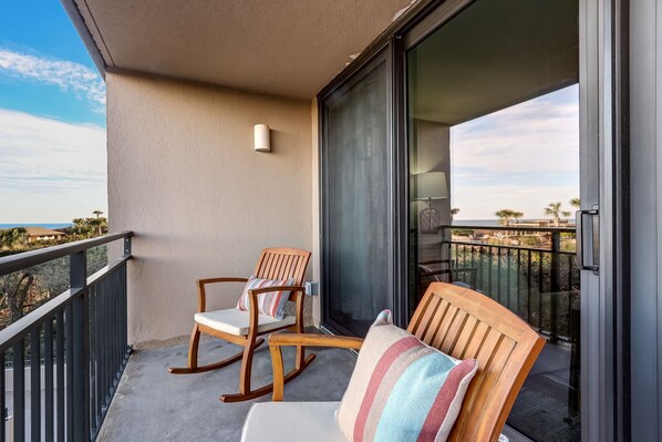 A balcony with two rocking chairs, a sliding glass door, and a view of the ocean.