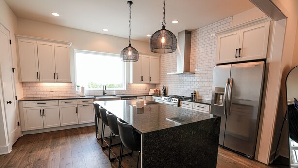 A modern kitchen with white cabinets, a large island with bar stools, a stainless steel refrigerator, and pendant lighting. - Luxe Nashville 3-bedroom Townhouse w/rooftop deck (Nashville)