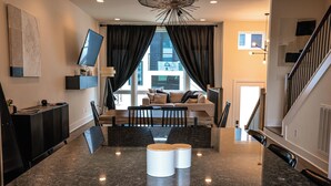 A modern living room with a large window, a flat-screen TV, a sofa, and a coffee table. - Luxe Nashville 3-bedroom Townhouse w/rooftop deck (Nashville)