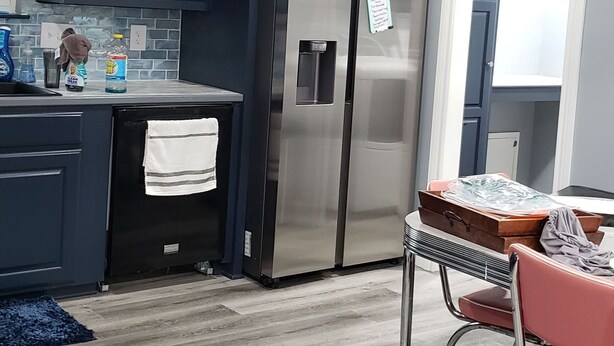 Una cocina moderna con armarios oscuros, electrodomésticos de acero inoxidable y una zona de comedor con una silla roja.
