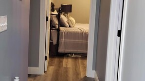 Un pasillo que da a un dormitorio con cama, mesita de noche y lámpara.