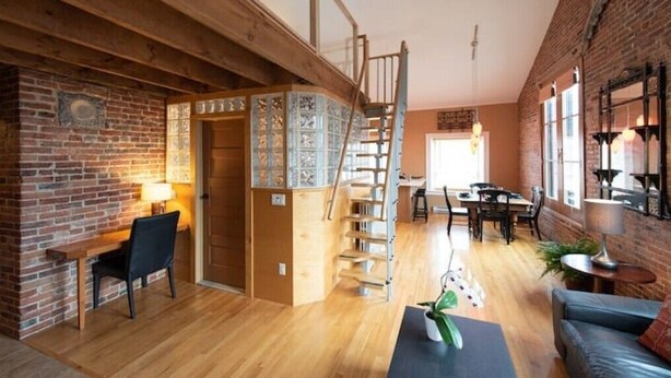 Une pièce chaleureuse avec un bureau en bois, un fauteuil confortable, un escalier et un coin repas comprenant une table et des chaises.