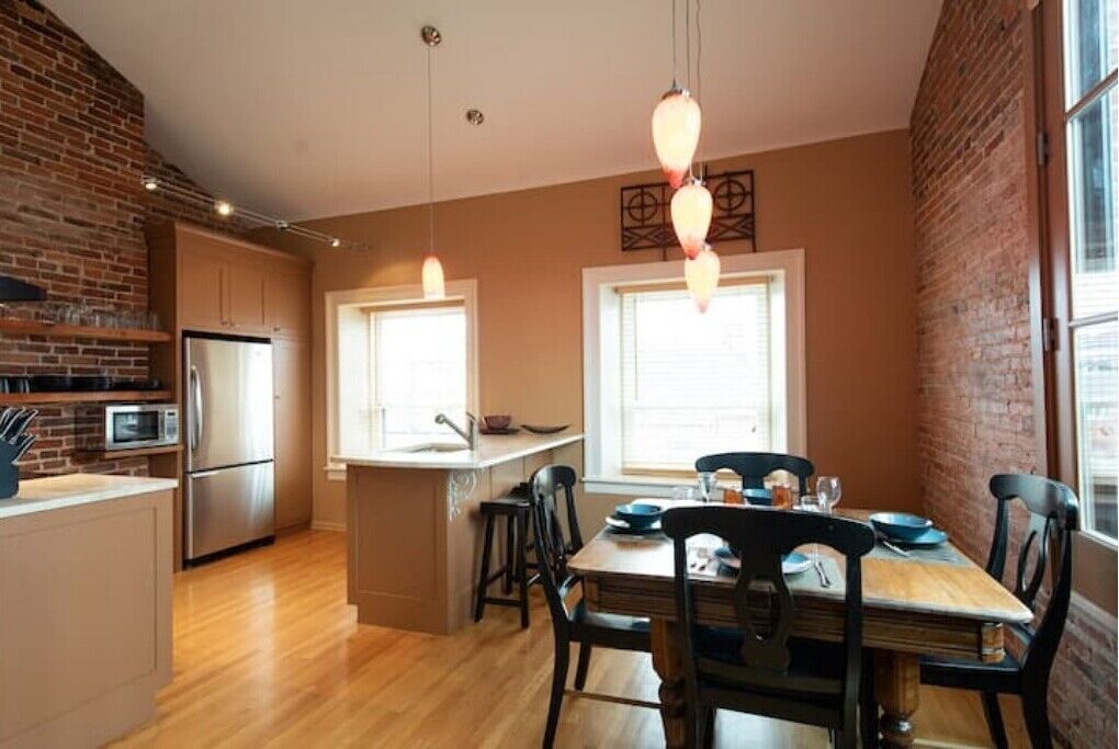 Una cocina moderna con pared de ladrillo, suelo de madera y comedor con mesa y sillas de madera.