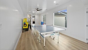 A ping pong table in a room with white walls, a ceiling fan, and a window. - Brand New Home! Roof Top Deck, Games for everyone, Private Pool (Hurricane)