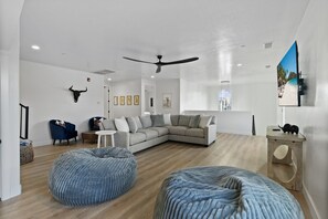 A modern living room with a sectional sofa, two bean bag chairs, a ceiling fan, and a mounted TV.