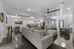 Una sala de estar moderna con un sofá seccional, una zona de comedor y una cocina al fondo.