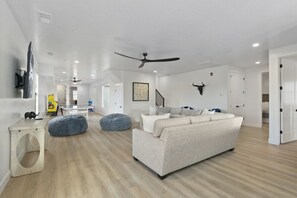 A modern living room with a sofa, two bean bags, a ceiling fan, and a bull head decoration. - Brand New Home! Roof Top Deck, Games for everyone, Private Pool (Hurricane)