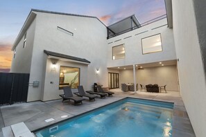 Un edificio moderno con piscina, sillones de descanso y zona de comedor.