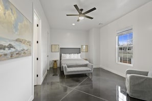 A bedroom with a bed, a grey sofa, a ceiling fan, a window with a view, and a painting on the wall. - Brand New Home! Roof Top Deck, Games for everyone, Private Pool (Hurricane)