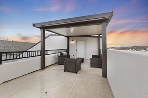 A covered outdoor seating area with a pergola, a door, and a view of the surrounding rooftops. - Brand New Home! Roof Top Deck, Games for everyone, Private Pool (Hurricane)