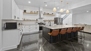 A modern kitchen with white cabinetry, a central island with bar stools, and pendant lighting. - Brand New Home! Roof Top Deck, Games for everyone, Private Pool (Hurricane)