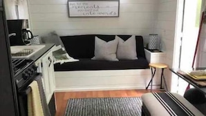 A compact kitchen with a stove, sink, and a black countertop. There is a black and white sofa with a rug in front. A small table and a lamp are on the right side. - LINVILLE Nostalgic Mountain Farm Glamping Camper on Wedding Venue, 10 acre farm  (Linville)